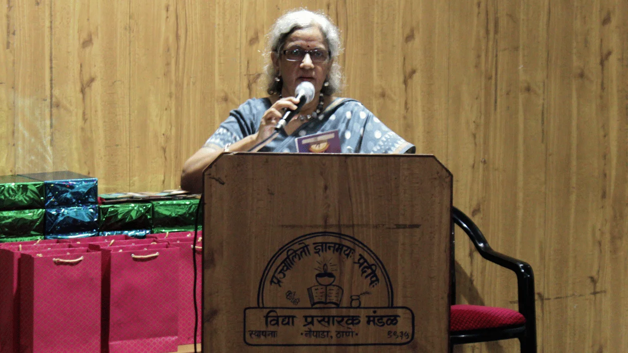 Woman addressing the audience from a wooden podium during a community event.